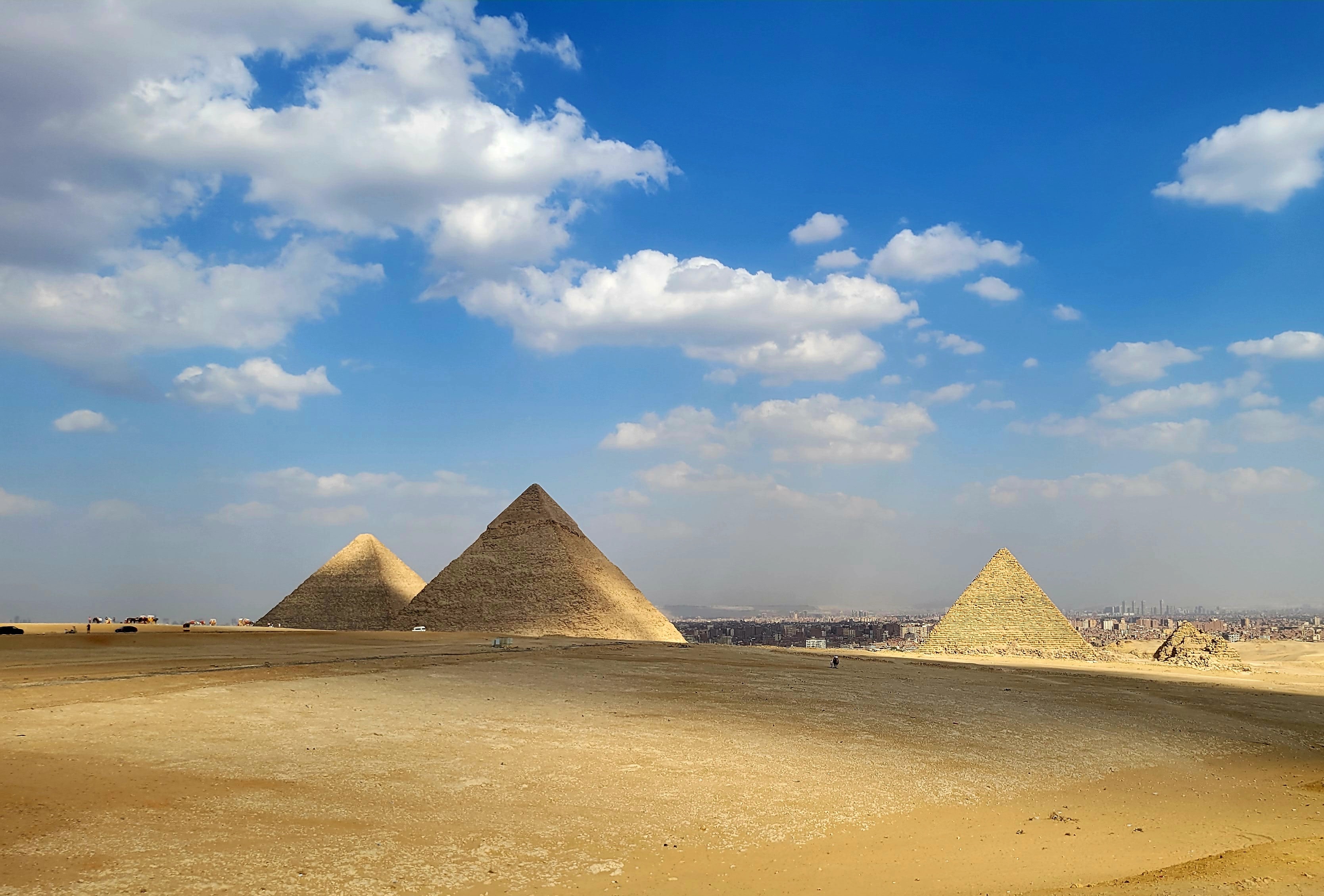 The three Great Pyramids of Giza against a blue sky with Cairo in the distance