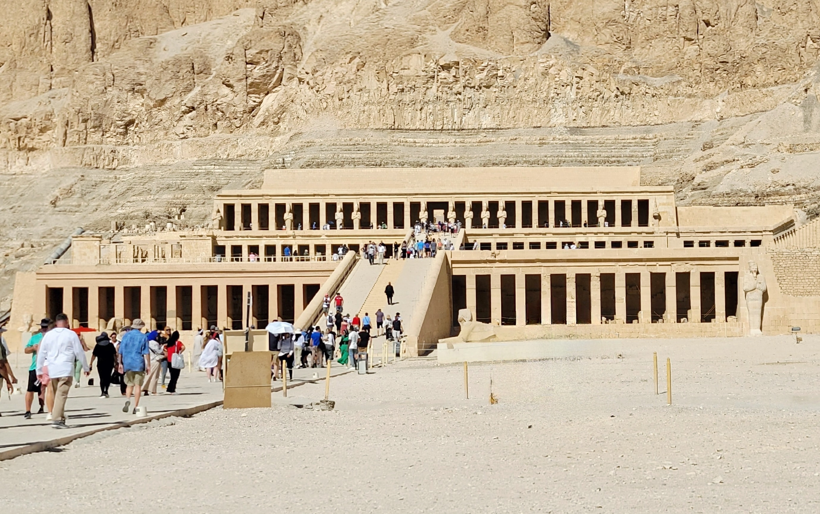 The Mortuary Temple of Hatshepsut with tourists visiting, set against the desert cliffs