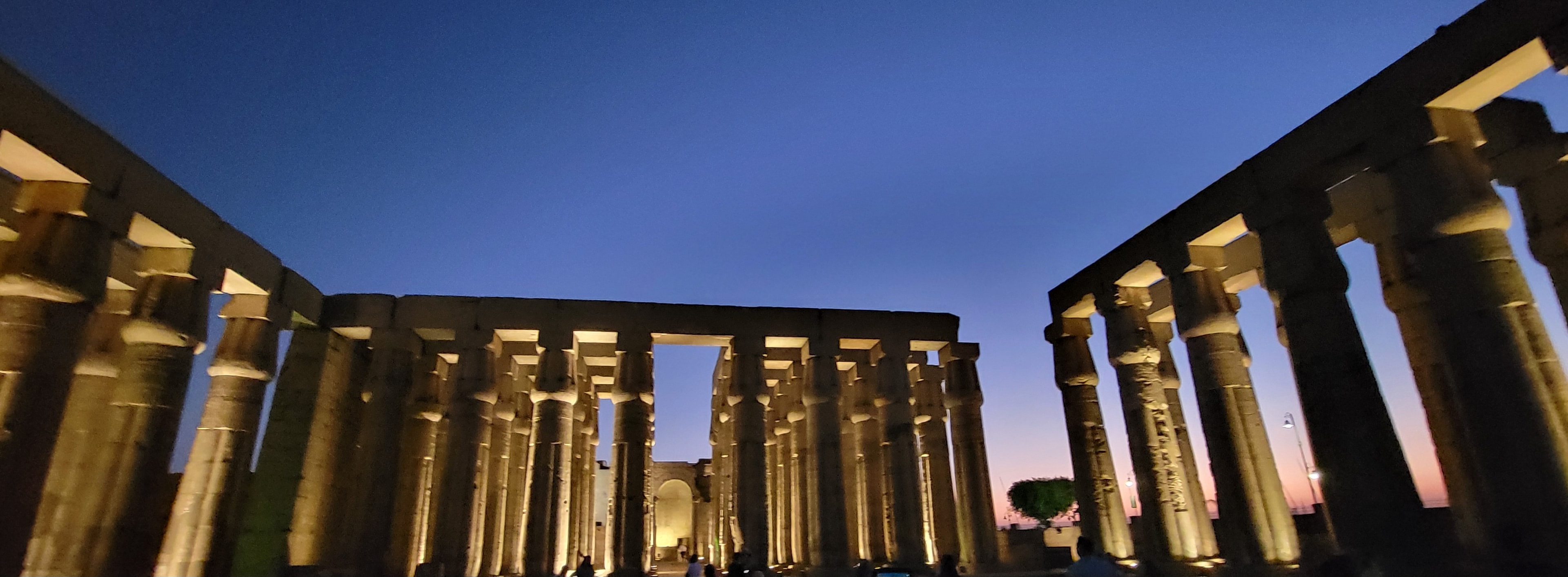 Luxor Temple illuminated at night, its colonnade glowing gold against a deep blue twilight sky