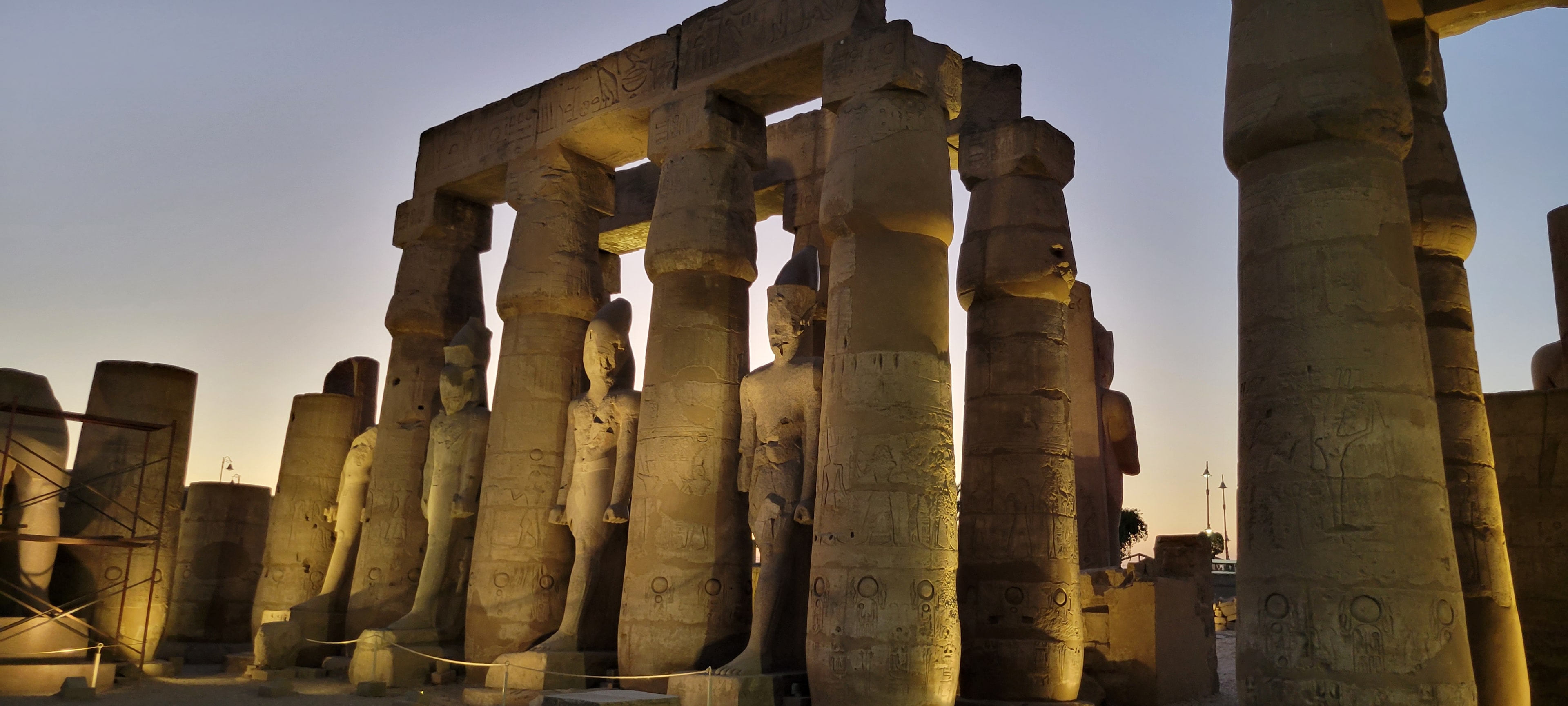 Colossal pharaoh statues and columns at Luxor Temple glowing at dusk