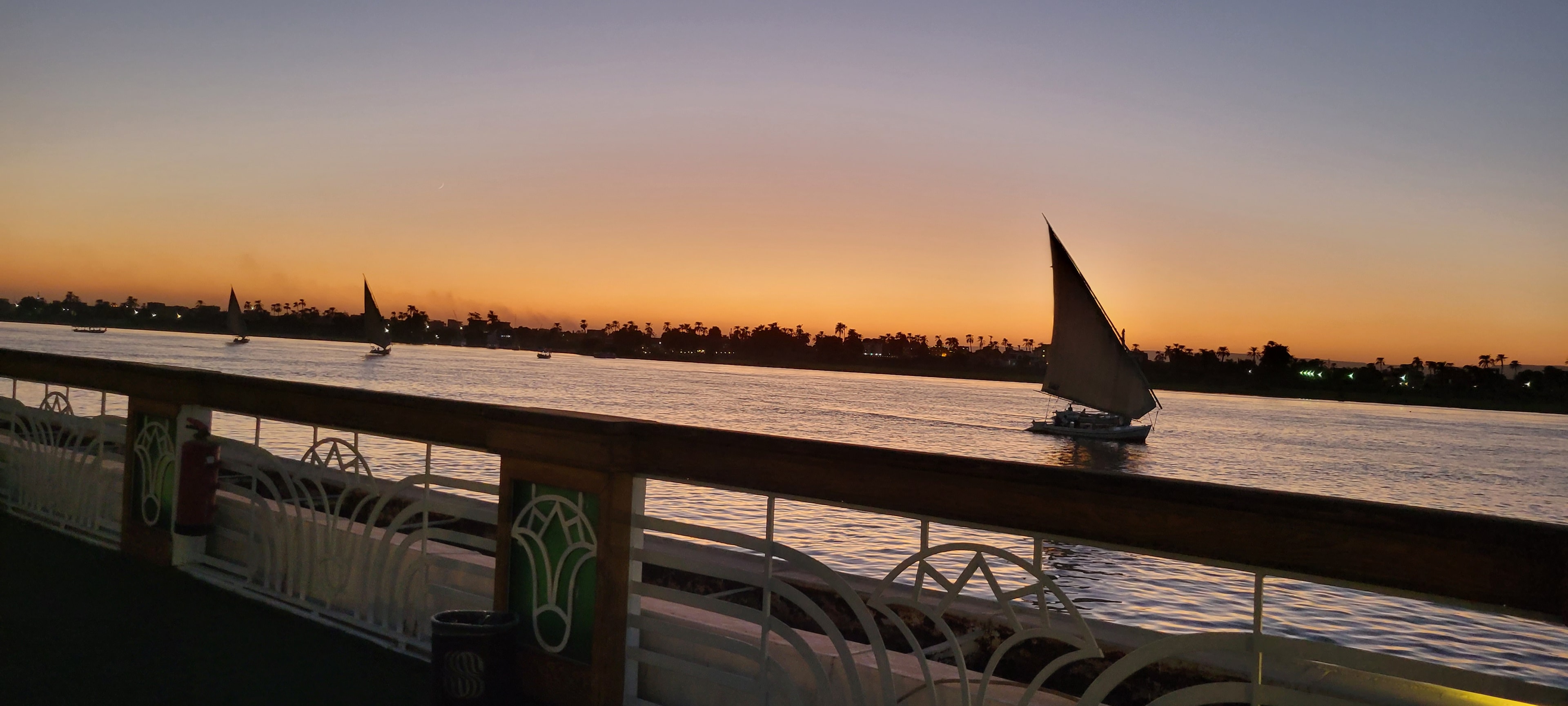 A felucca silhouetted against a golden sunset on the Nile, seen from the deck of a cruise ship