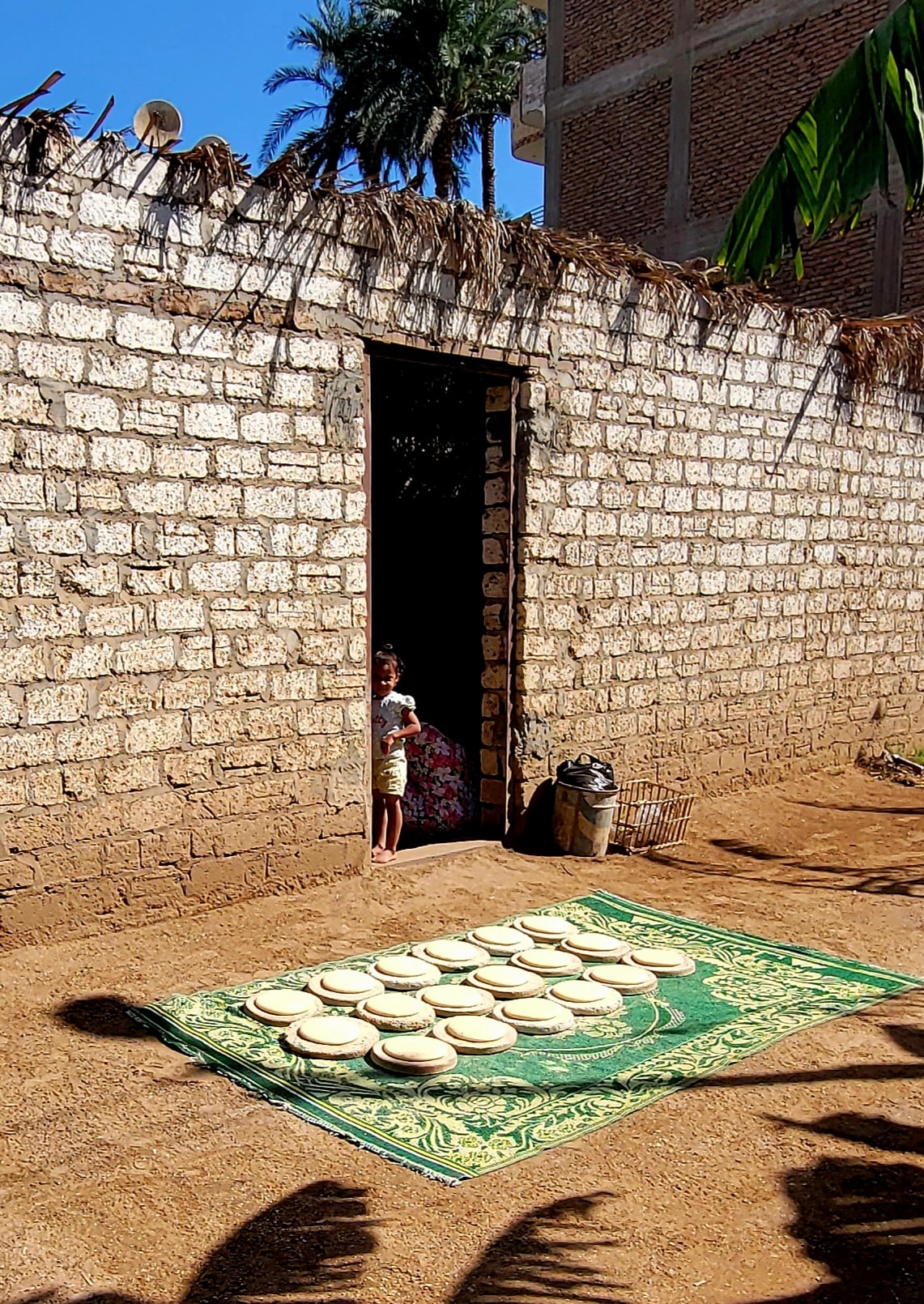 Rounds of flatbread drying on a green mat outside a stone village home