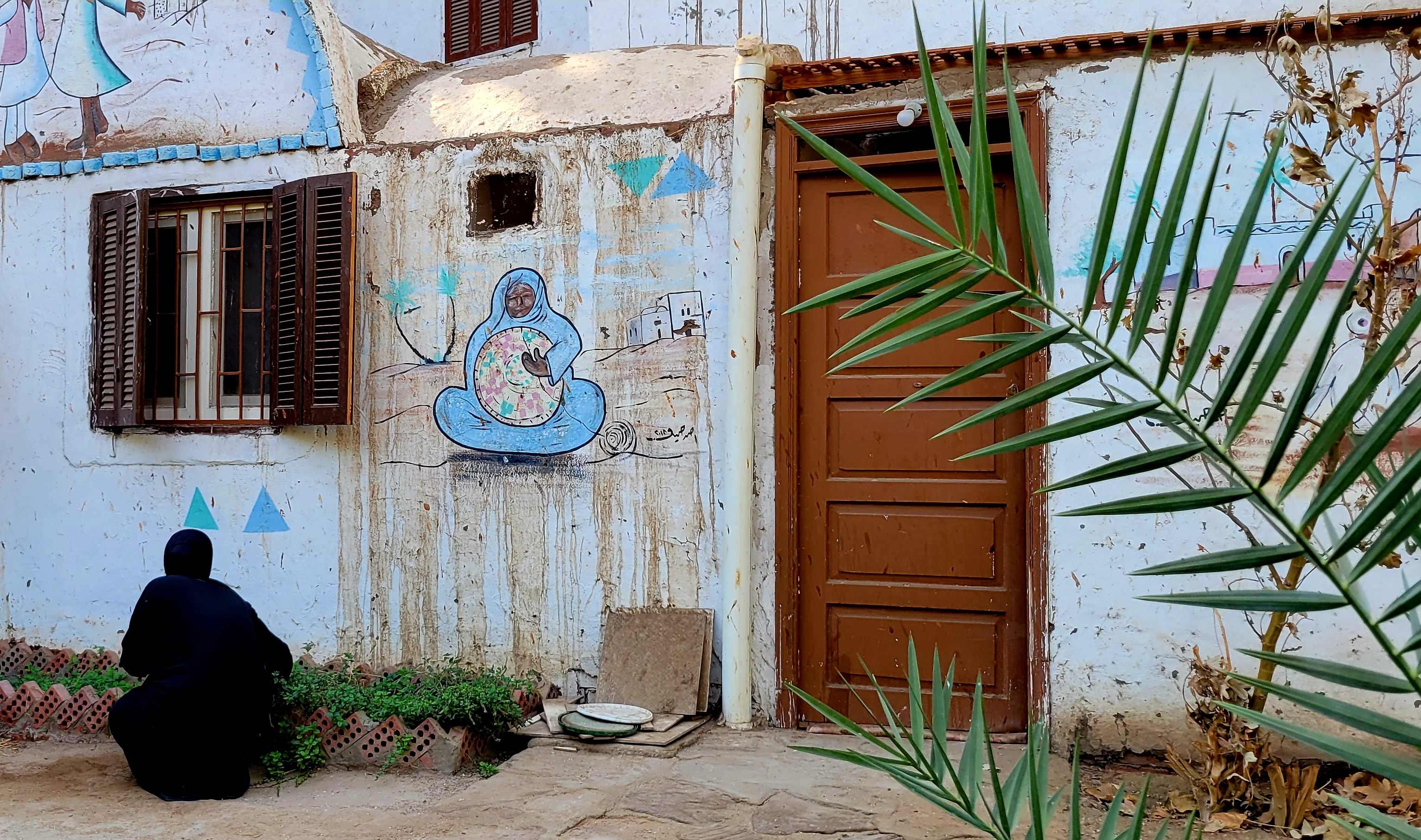 A woman in a Nubian village courtyard with colorful street art painted on the wall